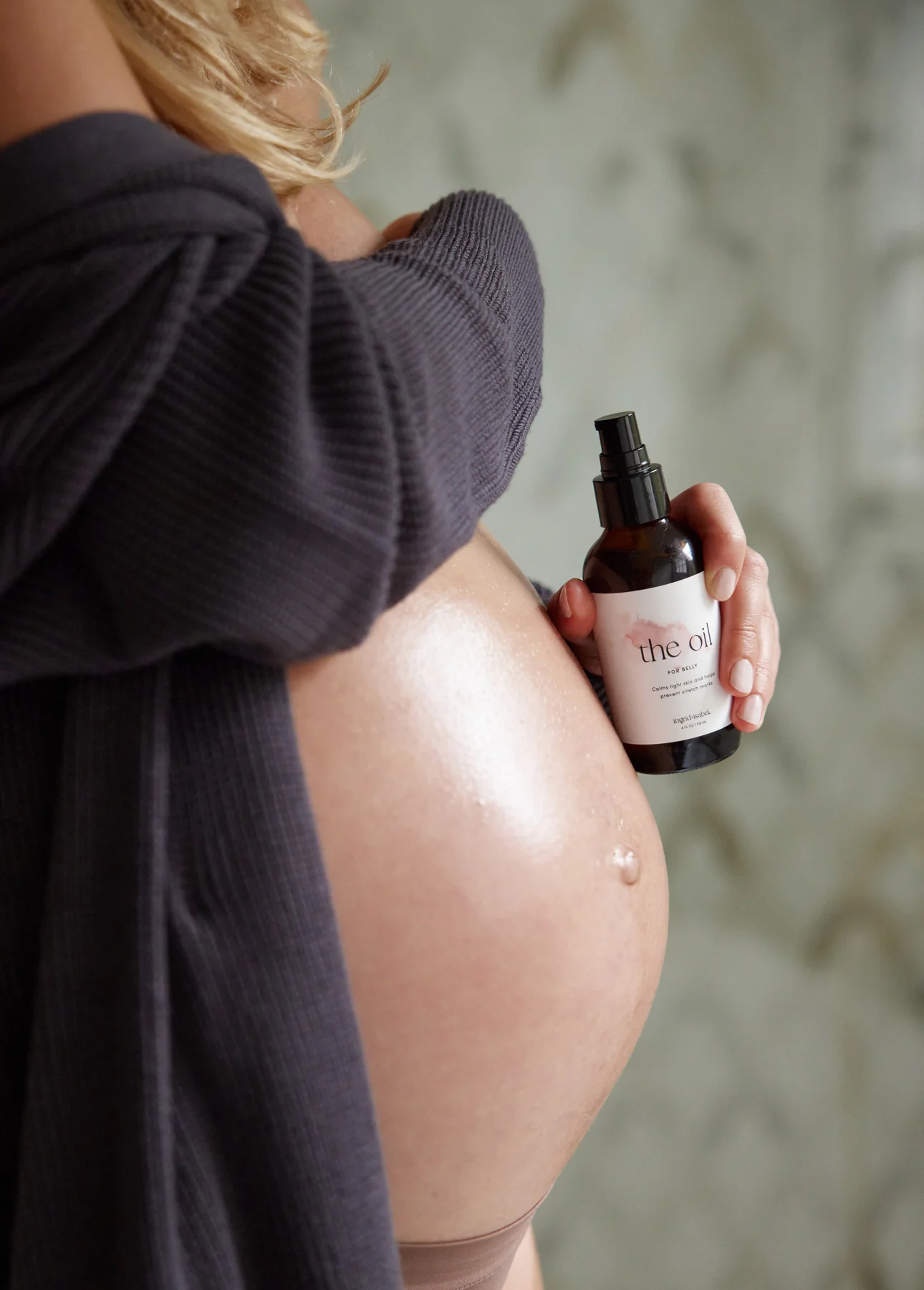 Side view of a pregnant belly and a hand holding a bottle of oil. 