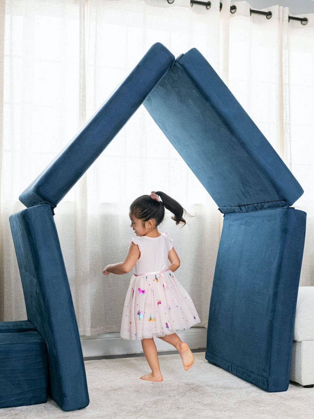 A girl runs through blue cushions stacked into a house shape