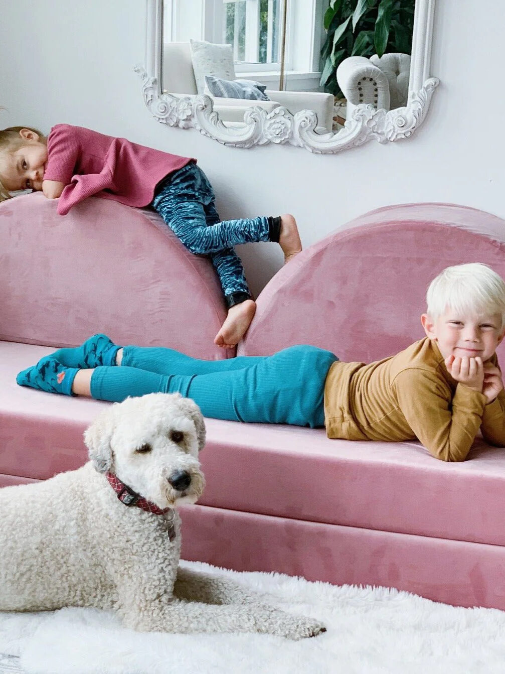 Two kids and a dog lounge around their pink play couch