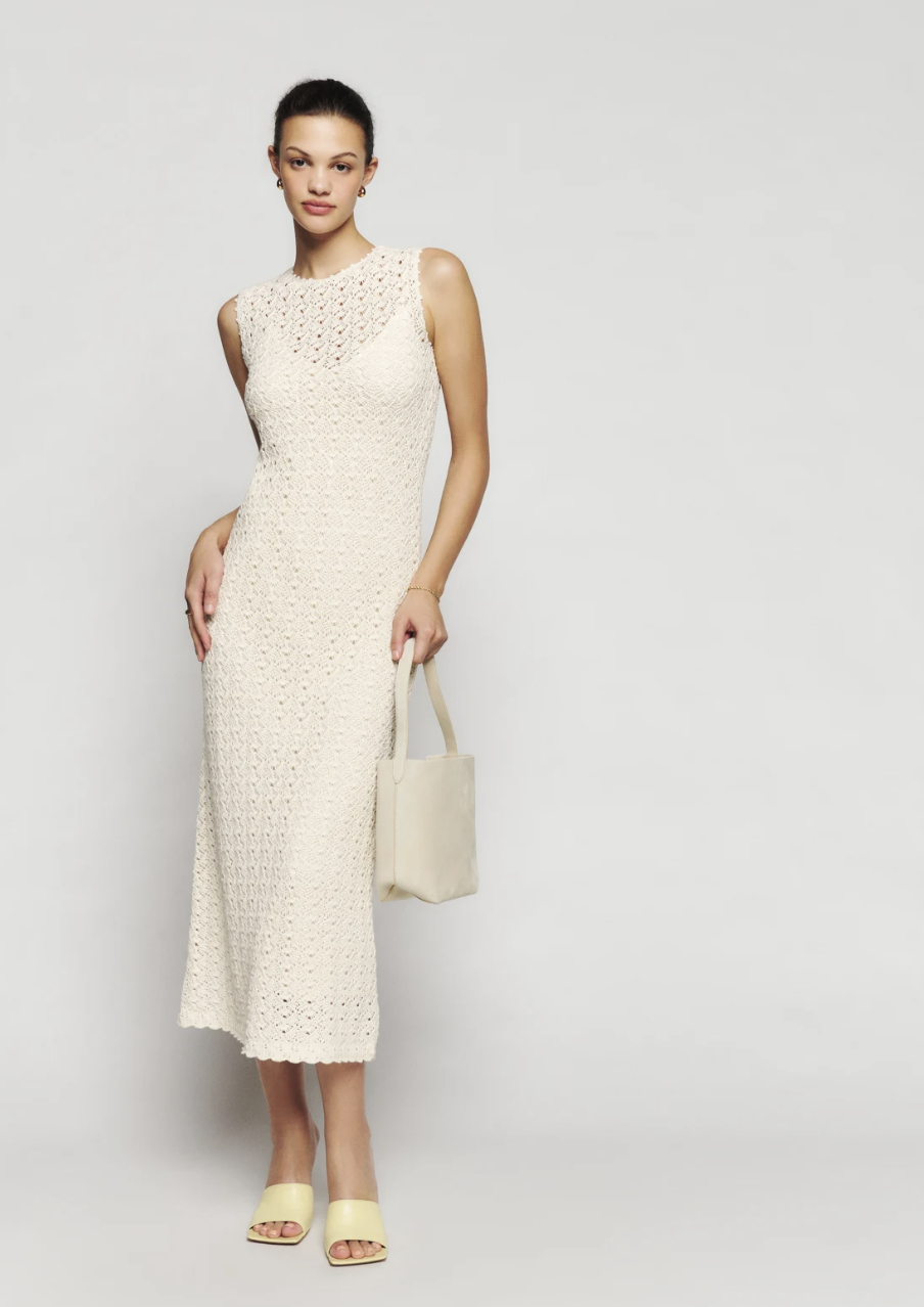 A model in a mid-length sleeveless ivory crochet dress