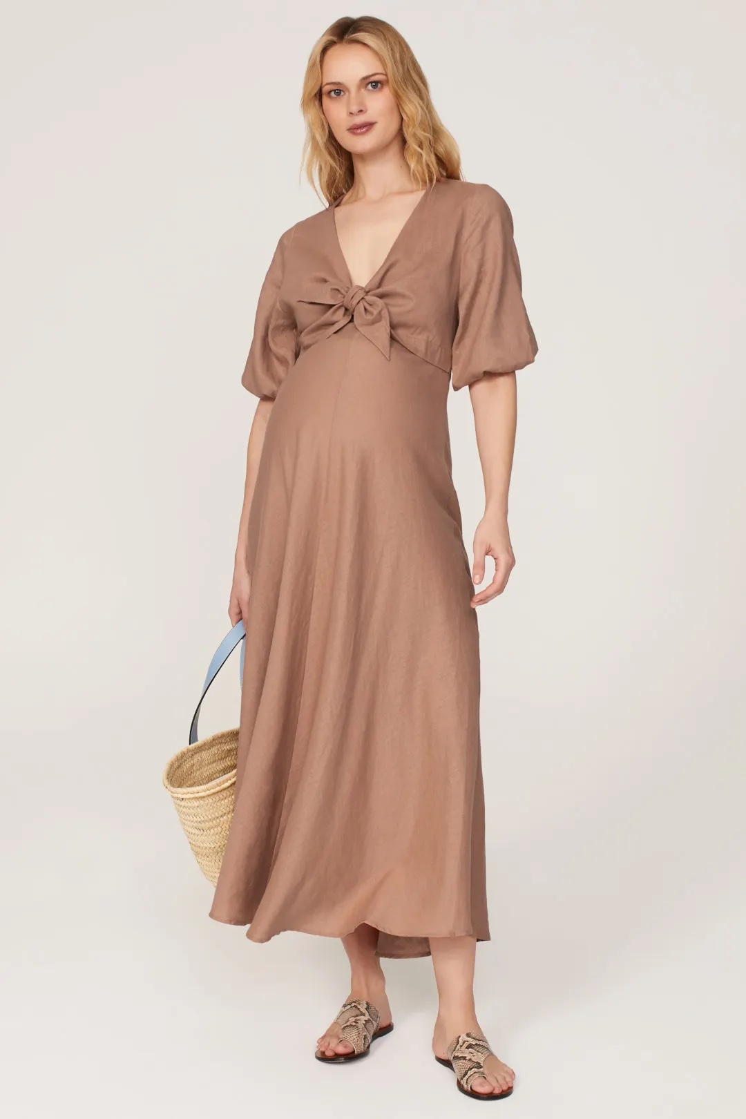A pregnant woman in a tan long dress with flutter sleeves and bow tie front.
