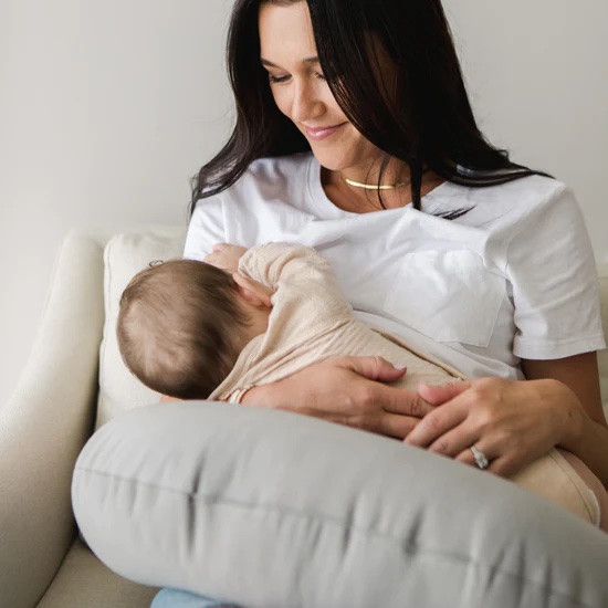A model nurses her baby using a gray support pillow.