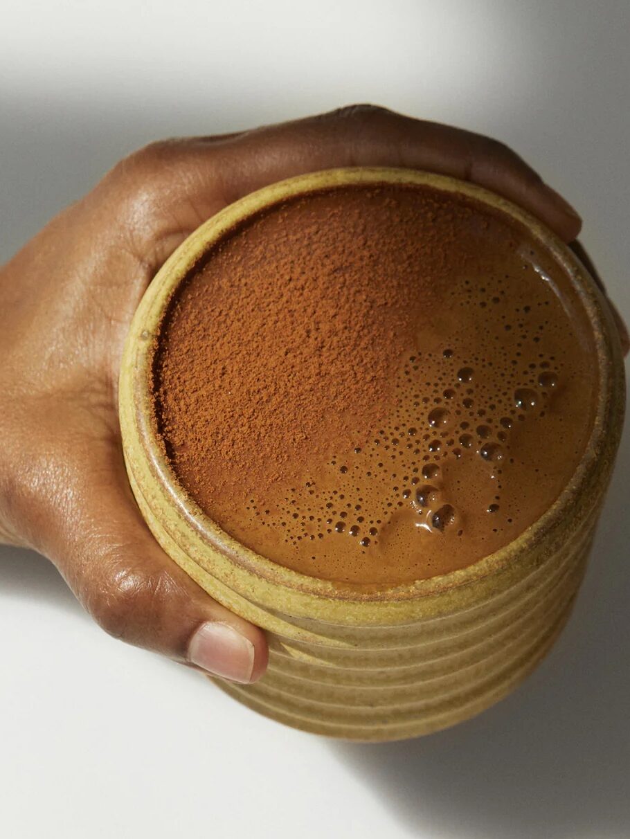 A hand holds a ceramic mug with Mud\Wtr in it