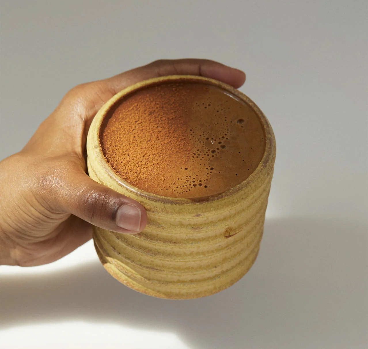 A close up of a hand holding a ceramic mug with brown liquid in it.