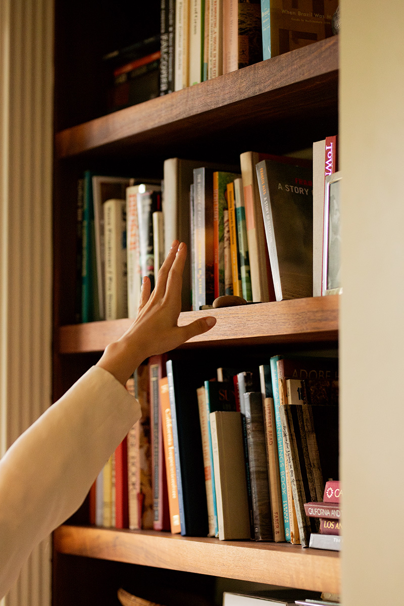 A person's hand selecting a book from a crowded wooden bookshelf filled with various books.