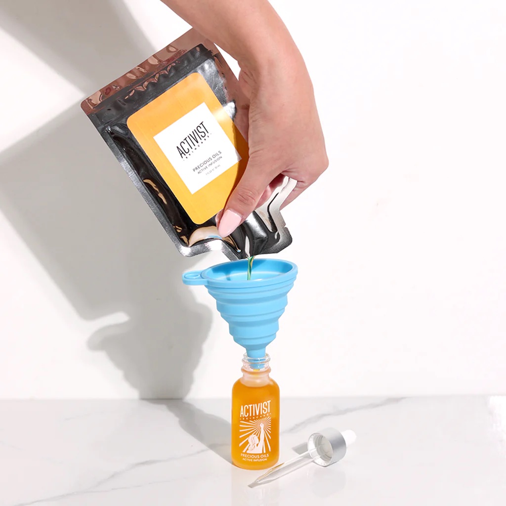 A hand pours from a refill pouch into a blue funnel into an Activist Skincare bottle.