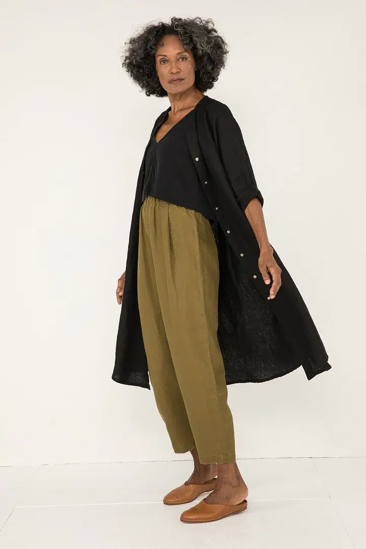 A model in tan slides, olive pants, black tank, and black open duster-length button down. 