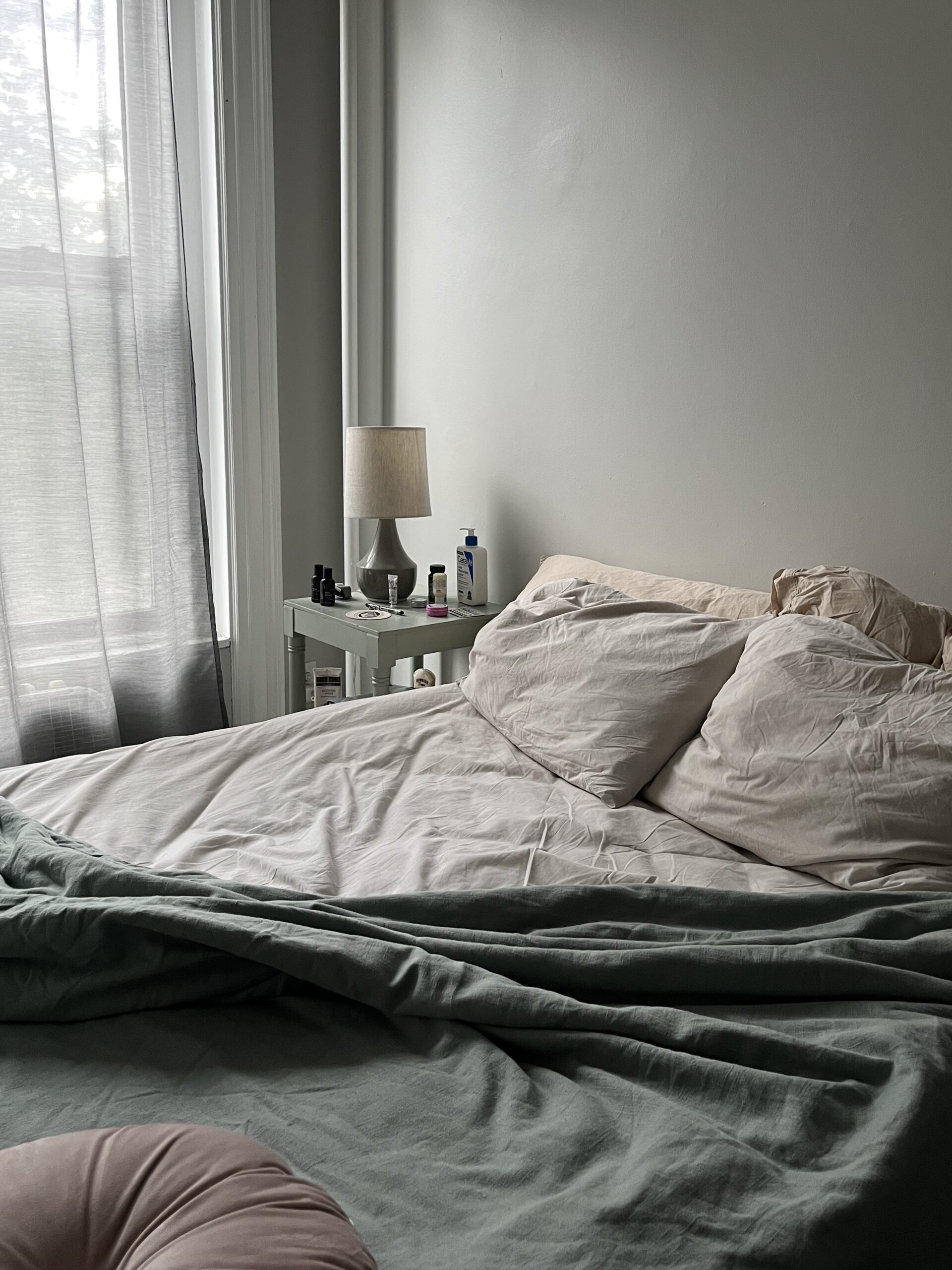 A photo of a slept-in bed in the morning next to the windows. 