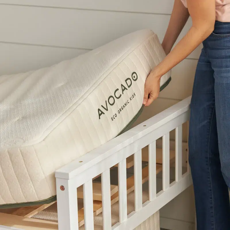 A close up of a twin mattress being set on a bed frame with the Avocado name visible on the side. 