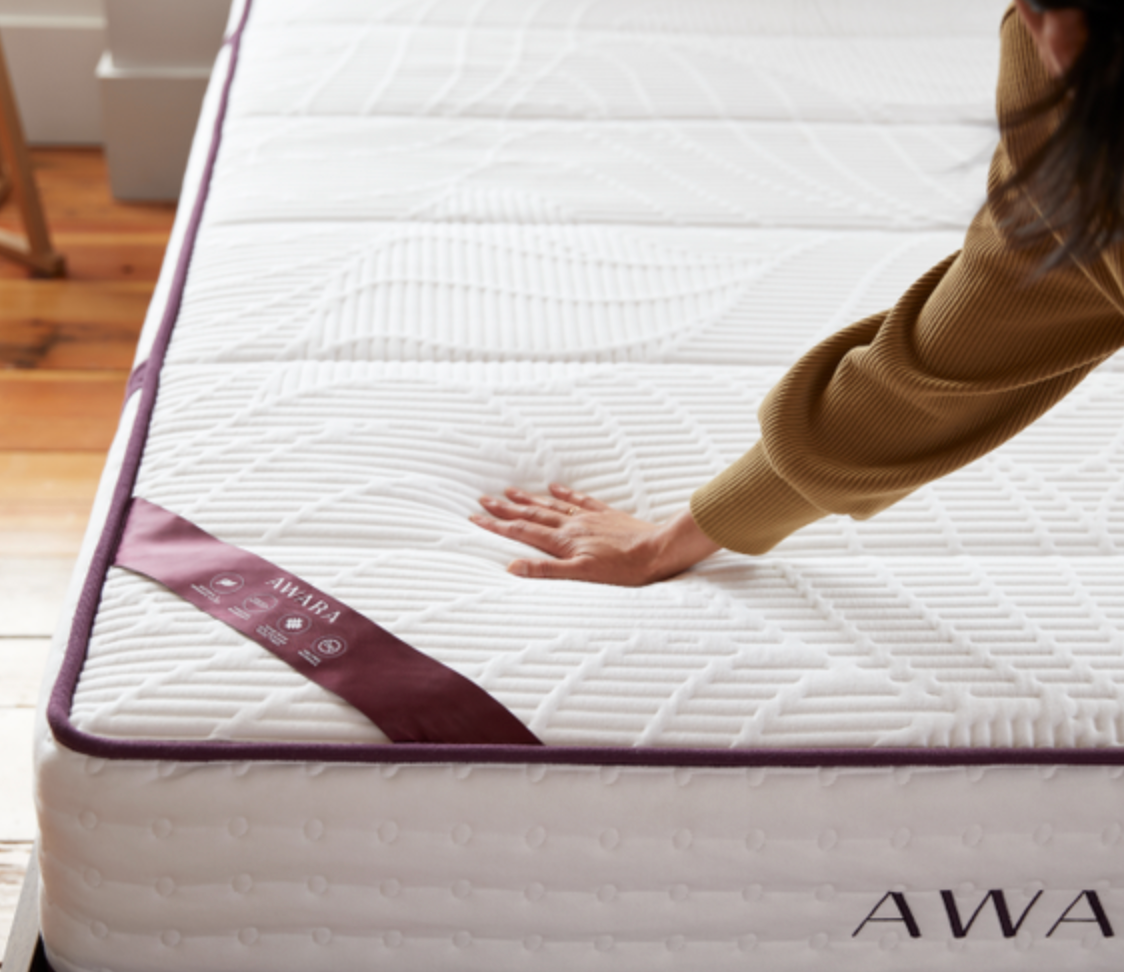A hand presses down on a mattress.