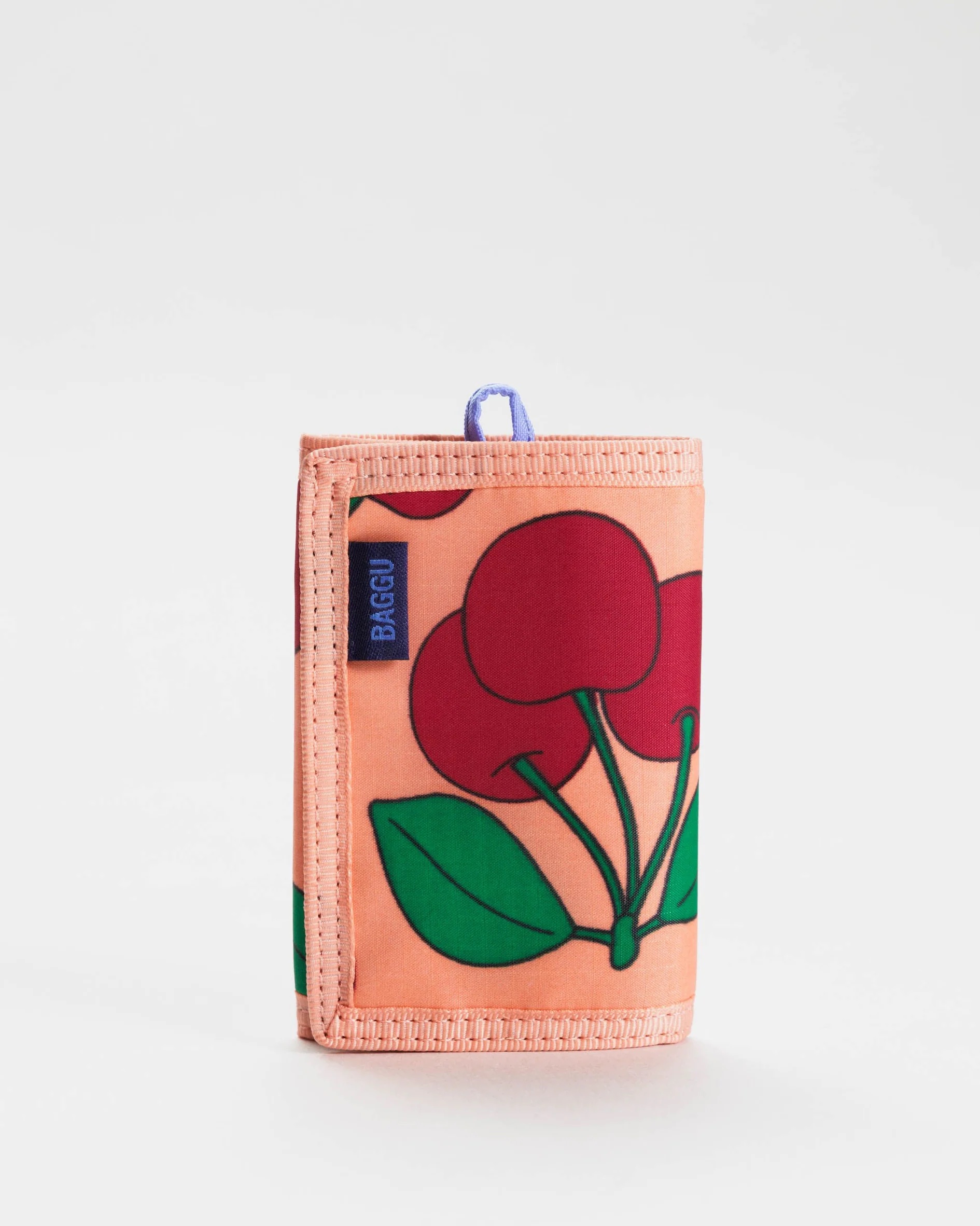 A peach-colored wallet with a cherry print on it and a Baggu tag. 