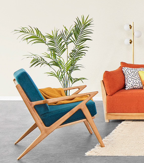 A wooden chair with teal cushions next to the corner of a wooden framed couch with orange cushions.