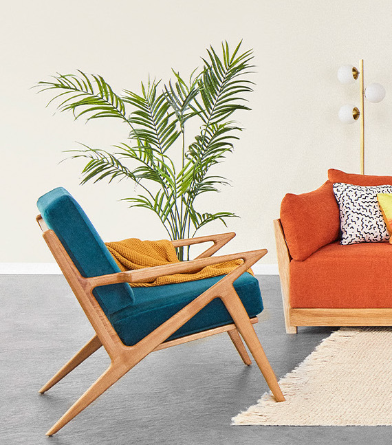 A wooden chair with teal cushions next to the corner of a wooden framed couch with orange cushions. 