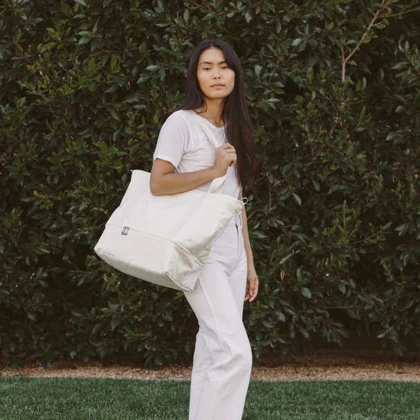 A model holds a carry on tote outside. 