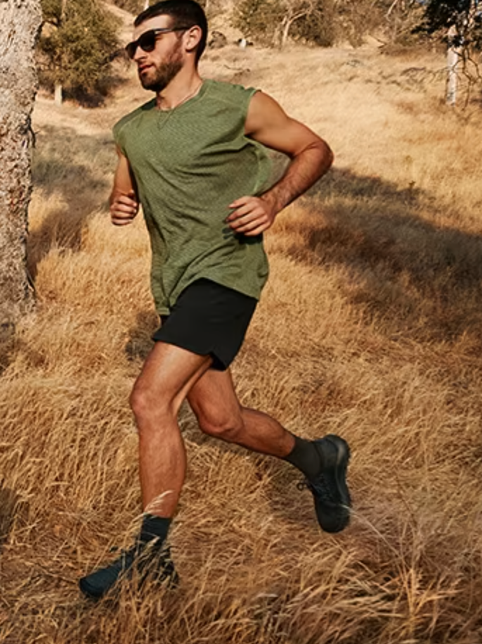 A man runs through dry grass in black Allbirds