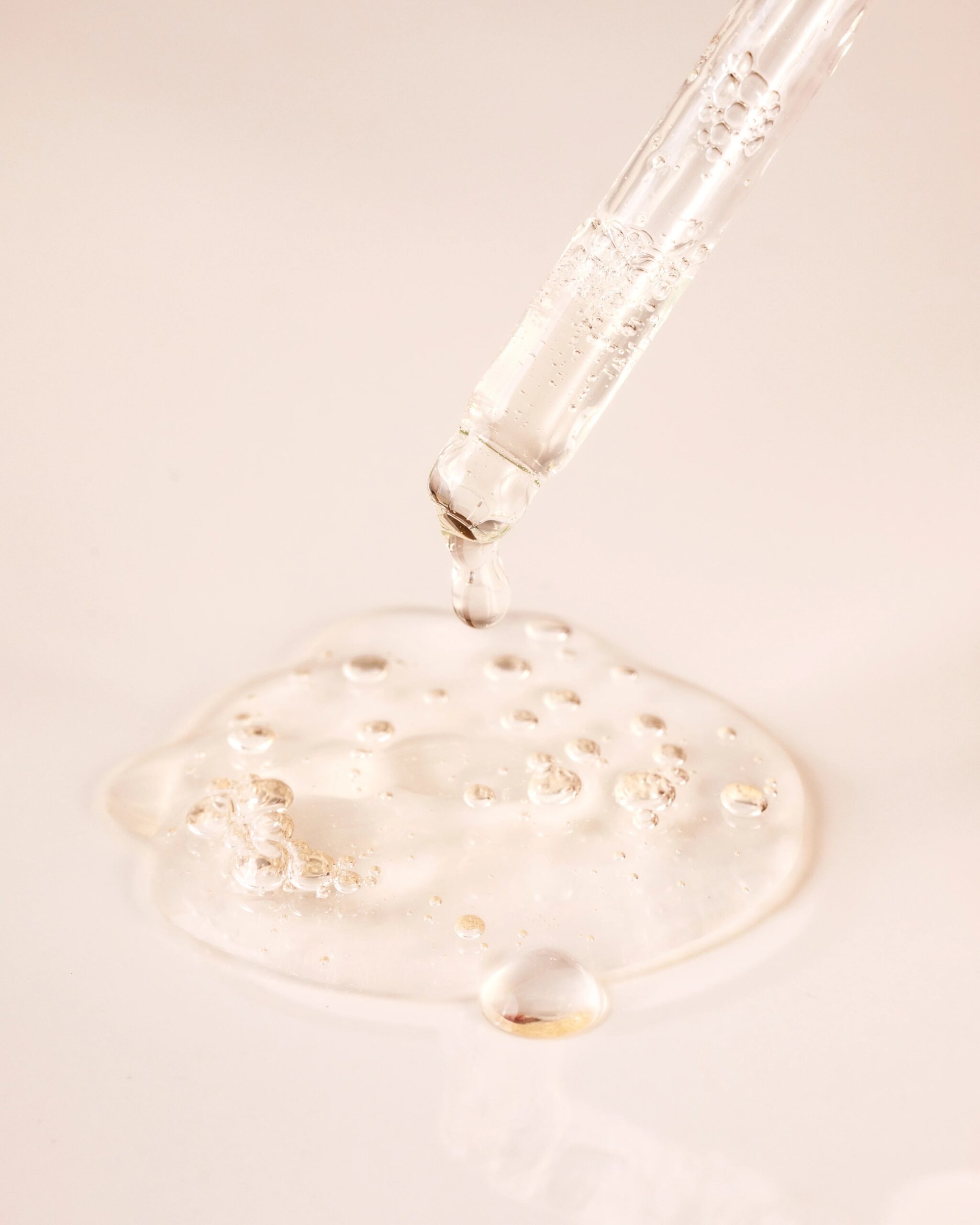 A close up of a dropper emptying serum into a puddle.