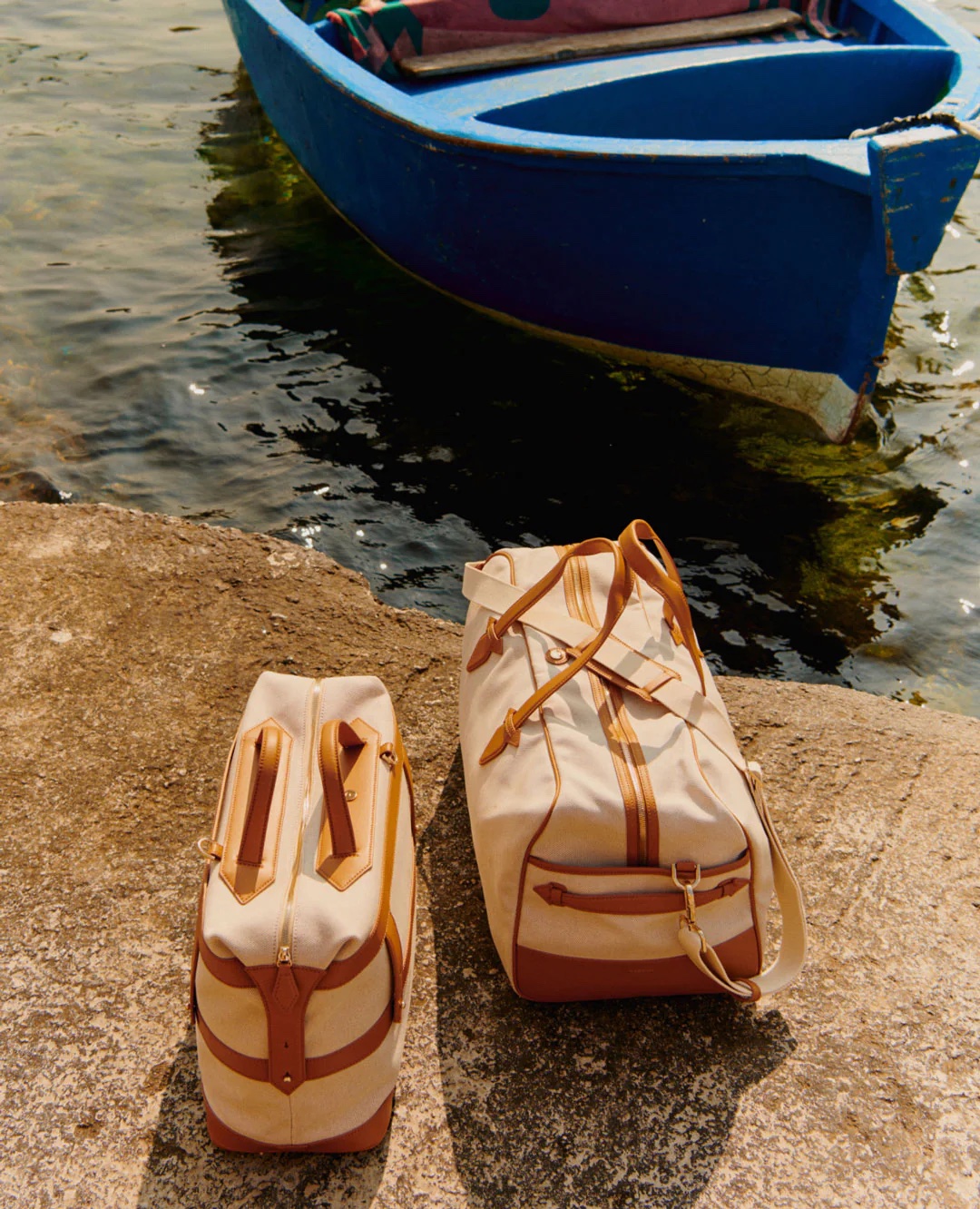 Two canvas bags sit on a stone dock next to a boat. 