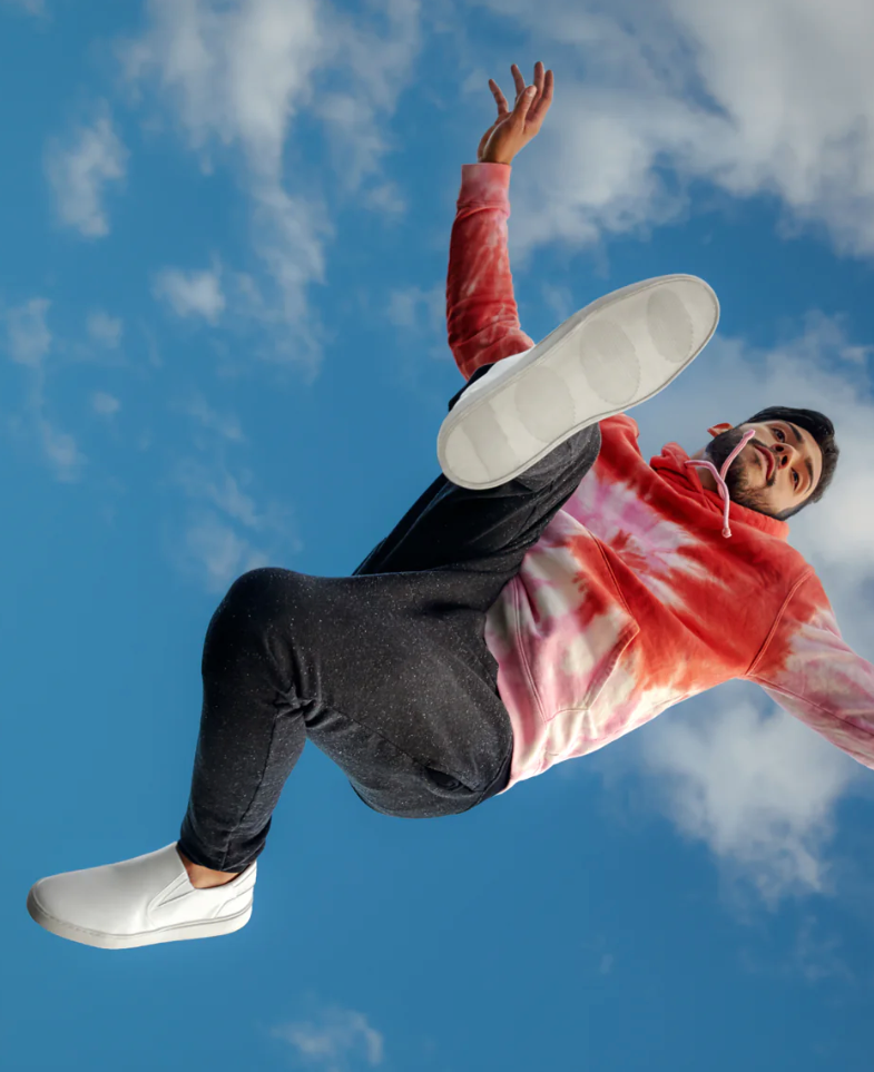 A man jumps over the camera wearing white slip ons. 