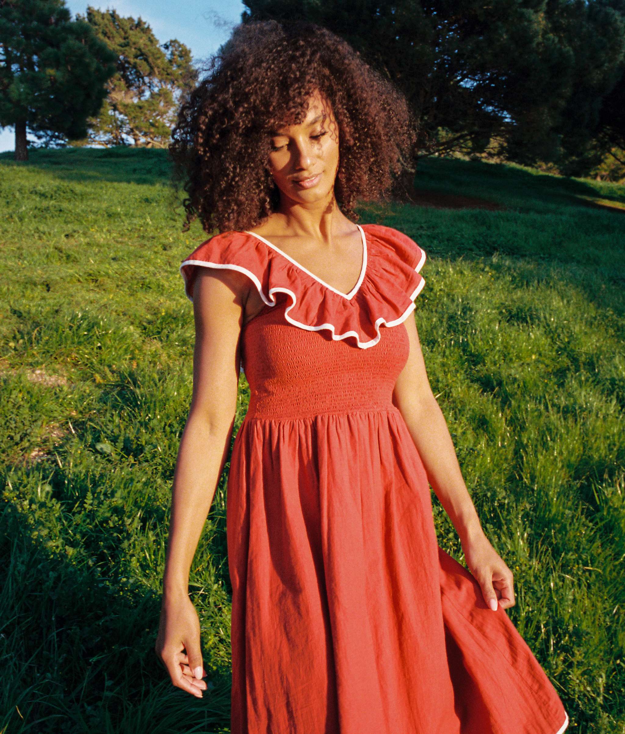 A model in a smocked red dress with ruffled neckline stands in a feel.