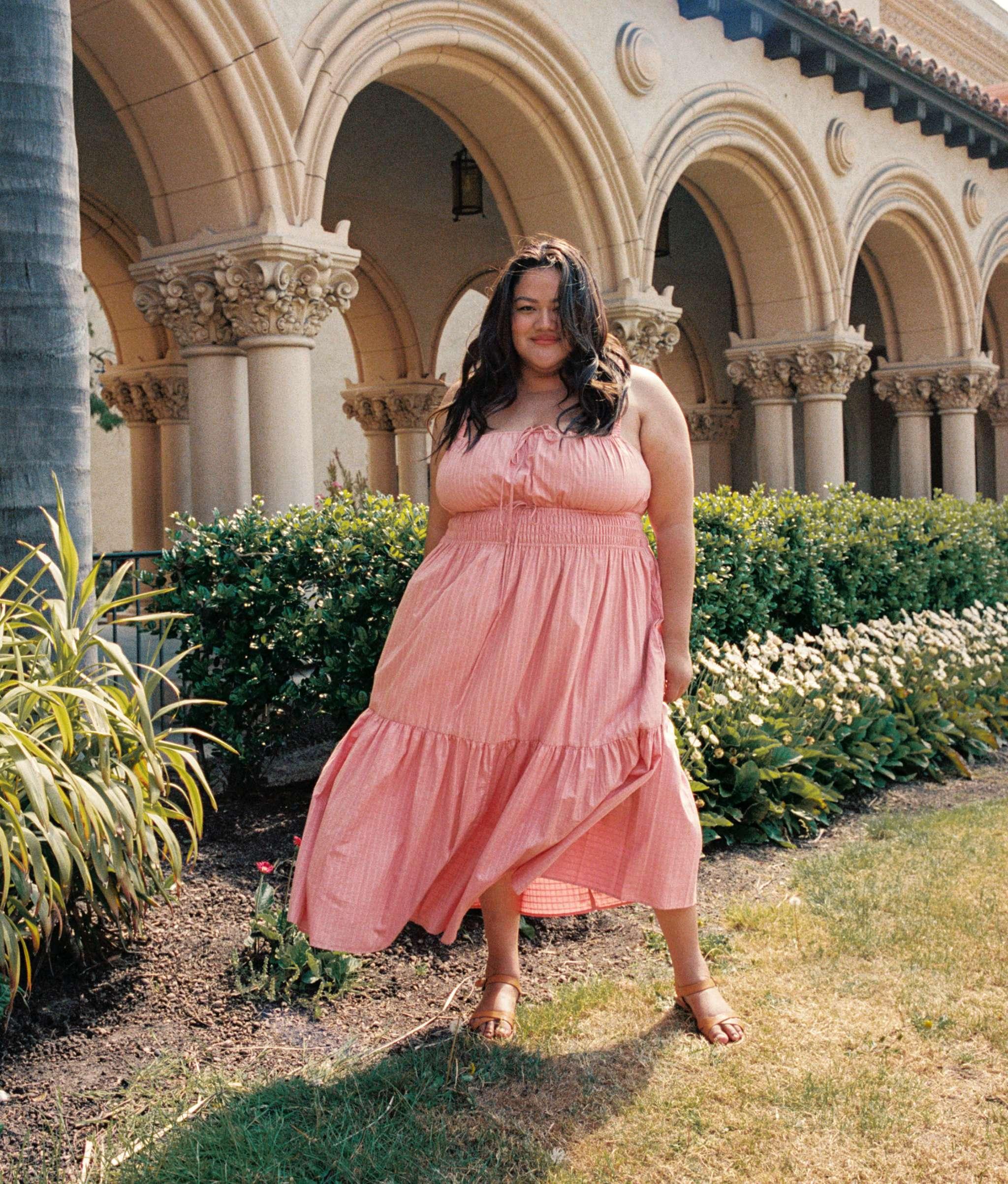 A model stands outside in a flowy pink dress.