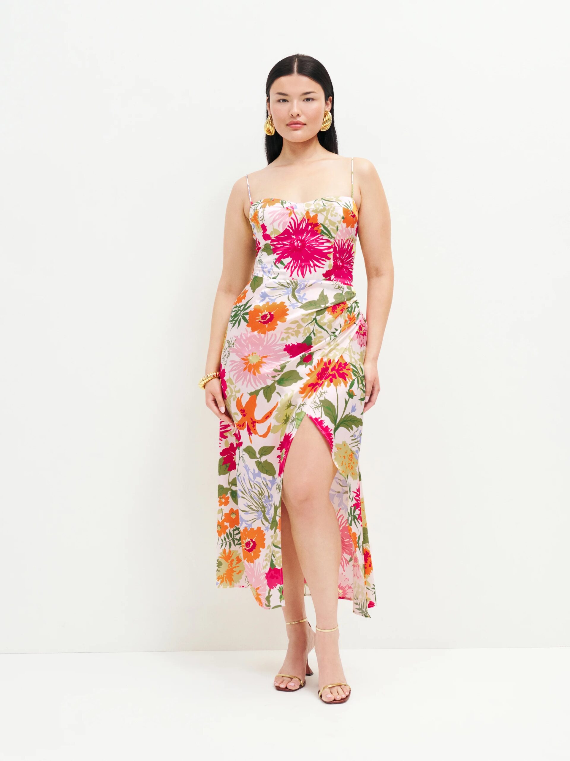 A model wears a floral spaghetti strap dress with a gathered waist and thigh slit.