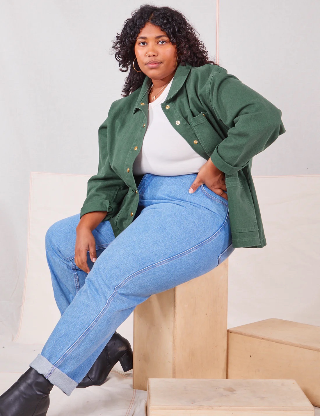 A model in jeans, boots, and open green button down with white tee.