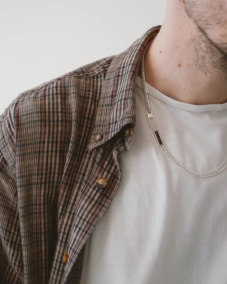 A close up of a silver chain and stone on a main's neck. 