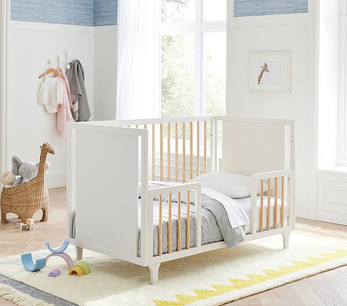 A converted toddler white bed with natural wood rails.