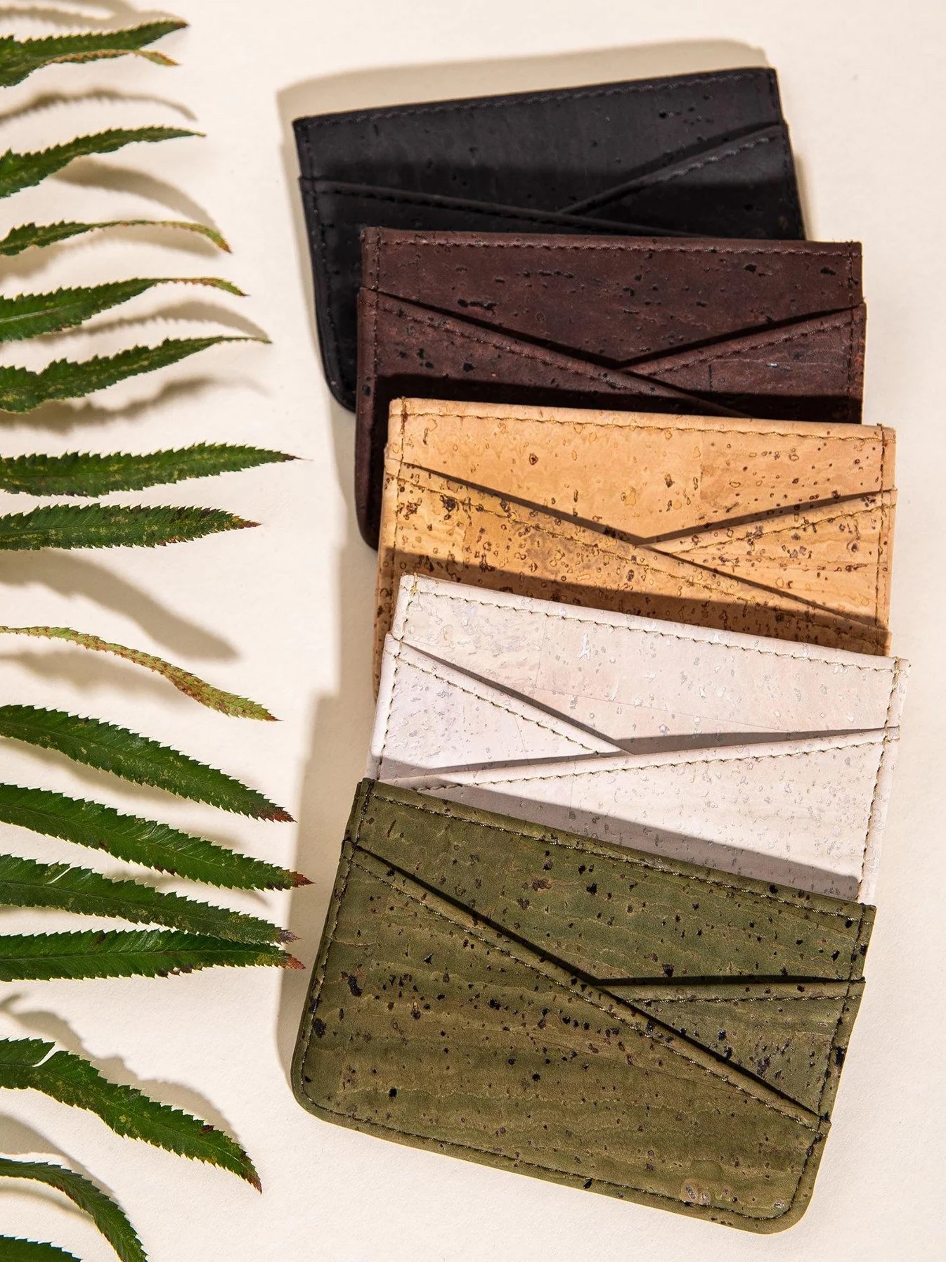 A line of different colored cork wallets on a table next to a plant. 