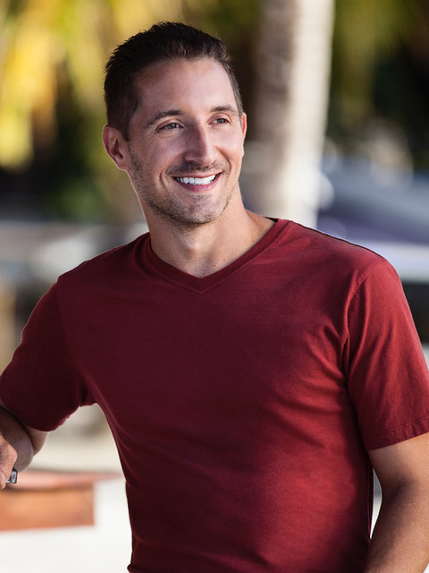 A man wearing a Fair Indigo red v neck shirt smiles.