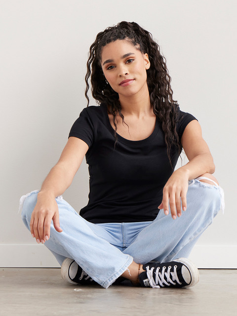 A woman wearing Fair Indigo jeans and black tee sits cross-legged.