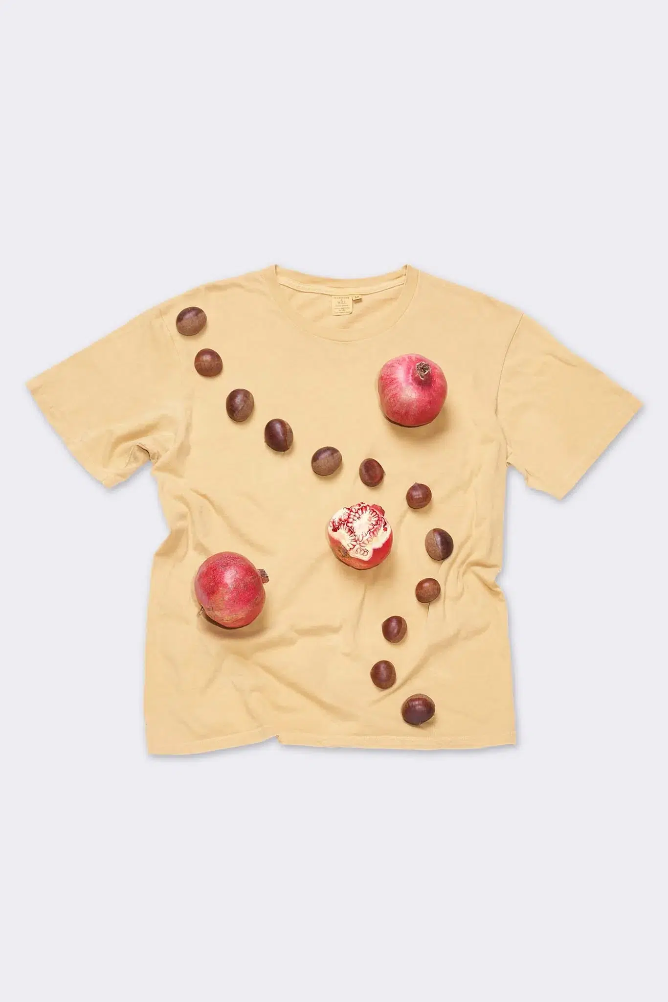natural dye yellow tee shirt flatlay with pomegranates and avocado seeds laying on top