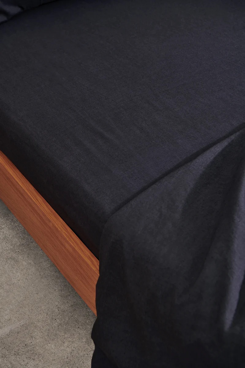 Black linen sheets on a made bed.