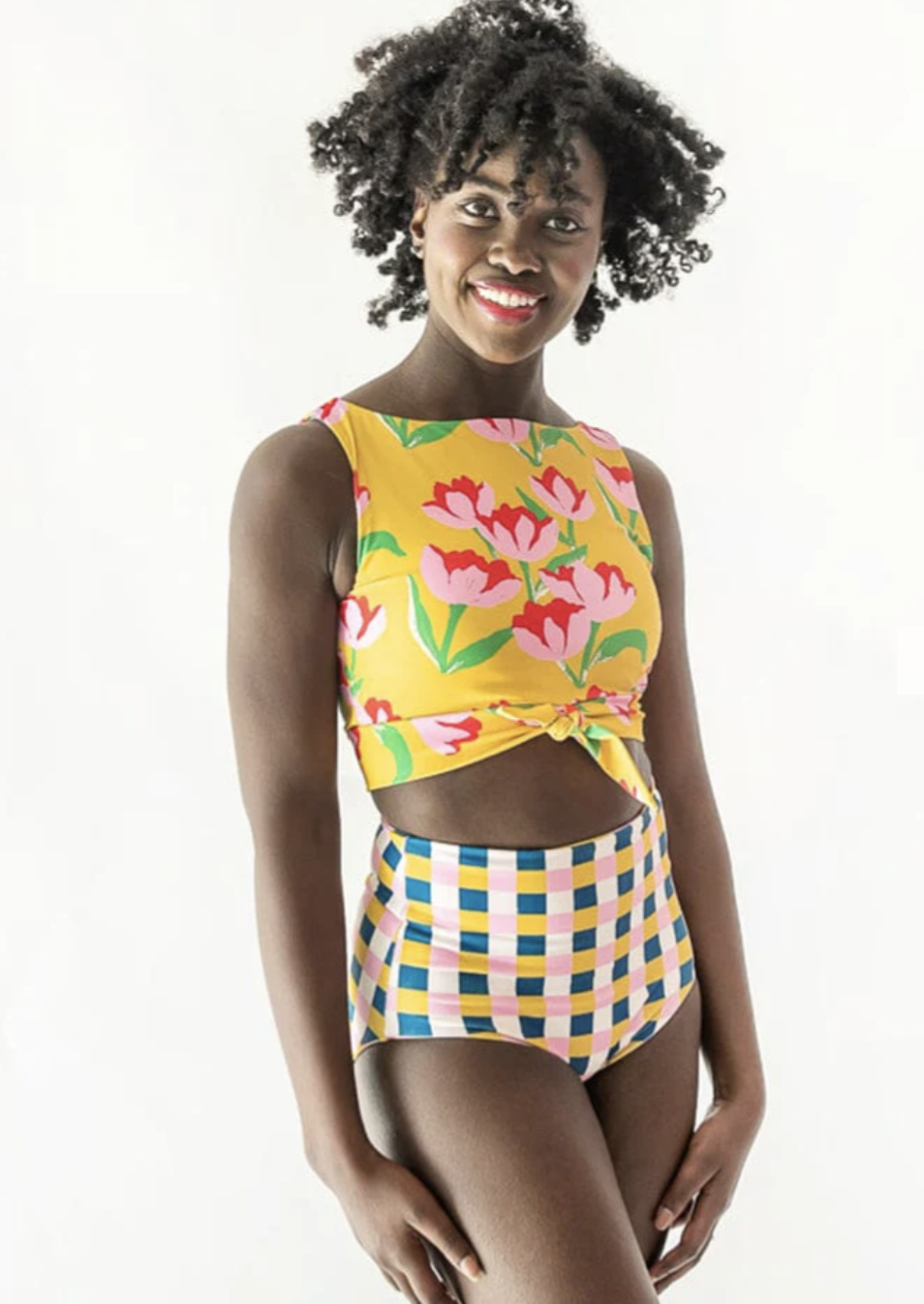 A model in a two piece swim suit with floral long line high necked tie-front top and plaid high waisted bottoms.