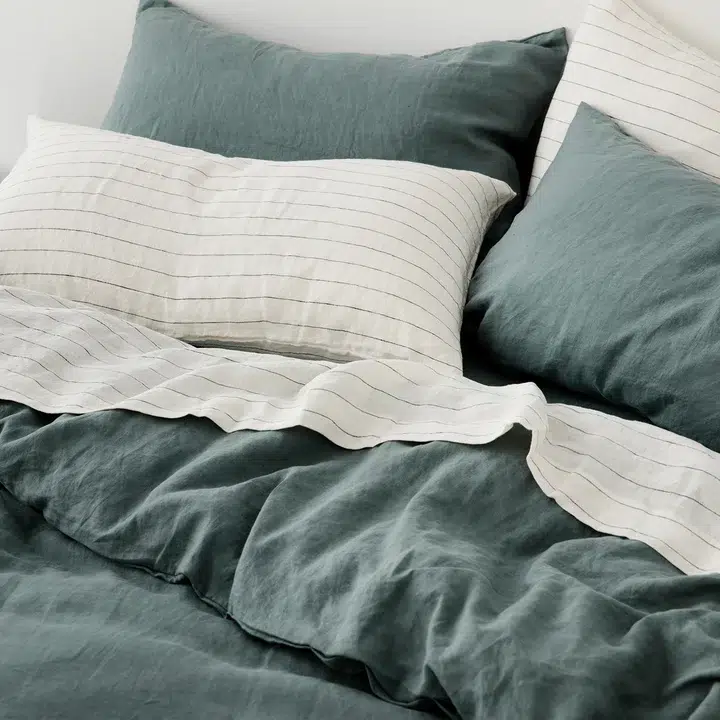 A bed made up in linen bedding in stripes and dusty teal. 
