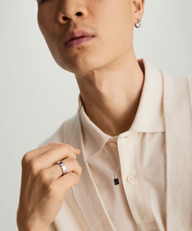 A man holds the silver chain of his pendant necklace away from his collar. 