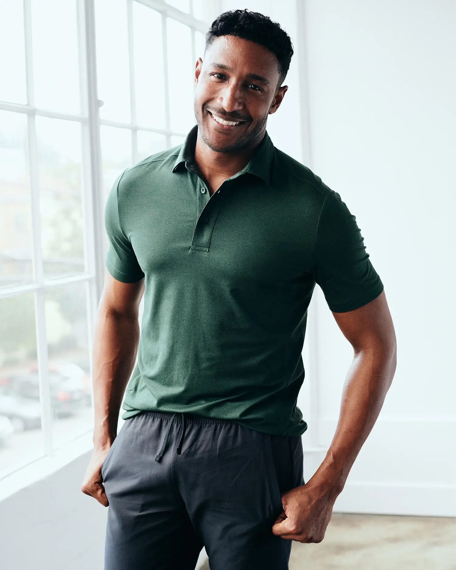 A model in a green fitted polo and dark gray pants.