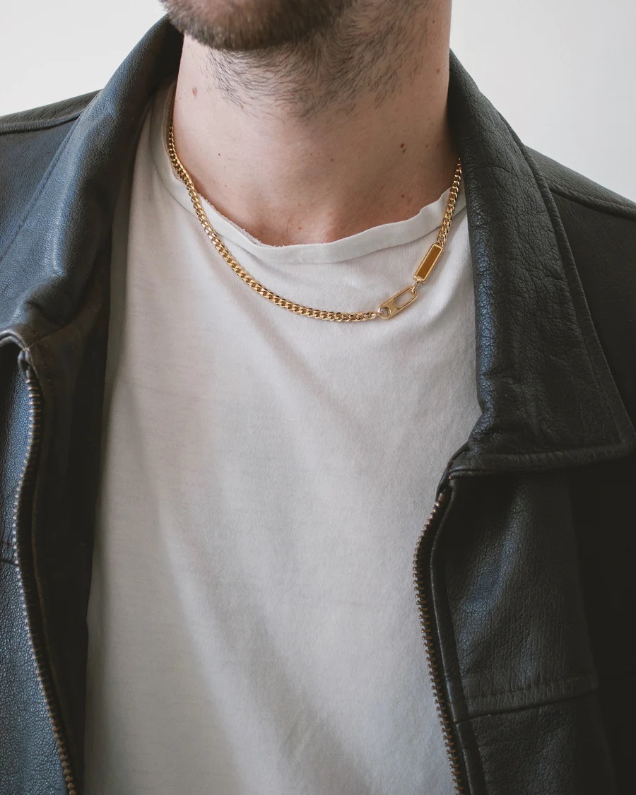 A close up of a gold chain and stone on a man's neck. 