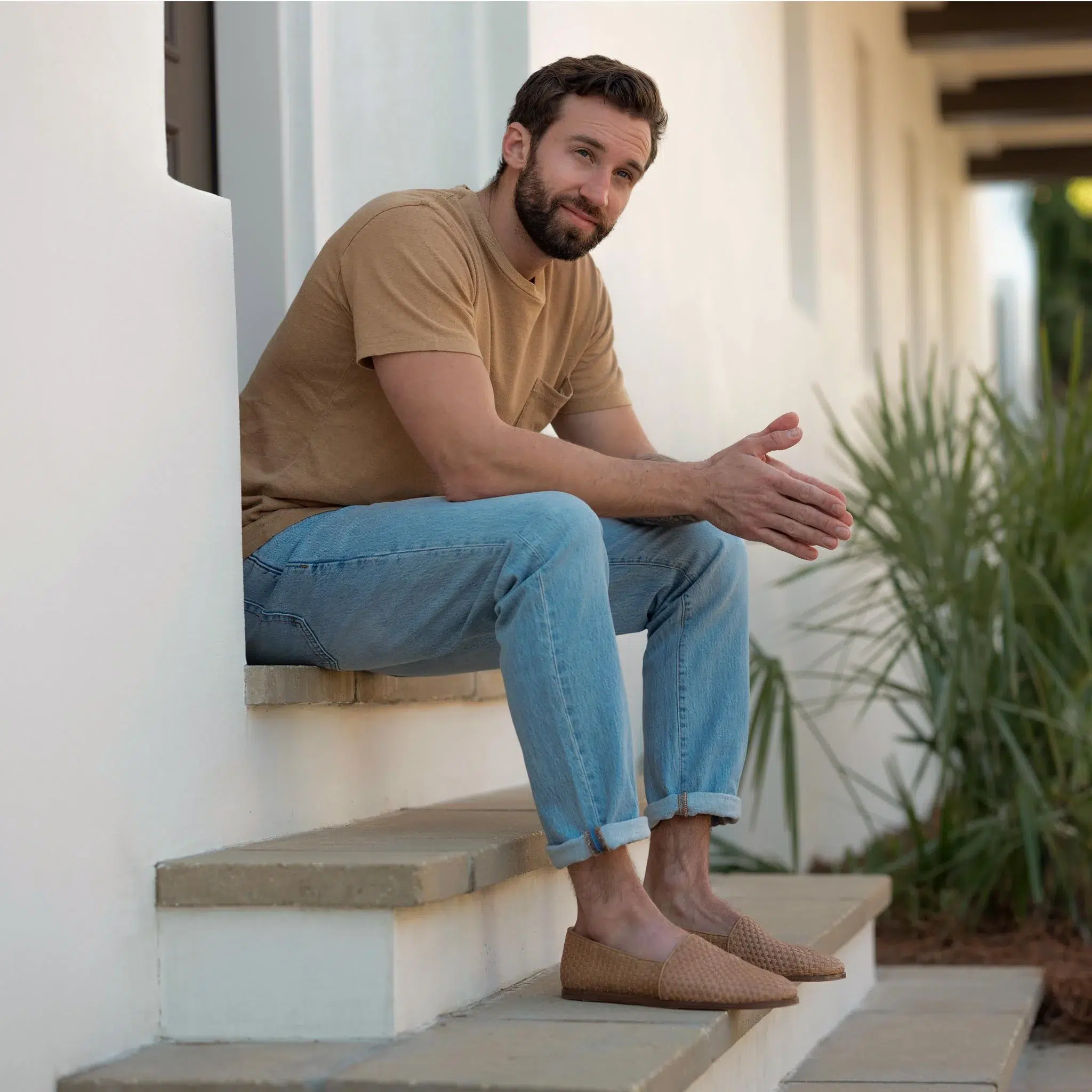 A model wearing a t-shirt, jeans, and slip on Nisolos sits outside. 