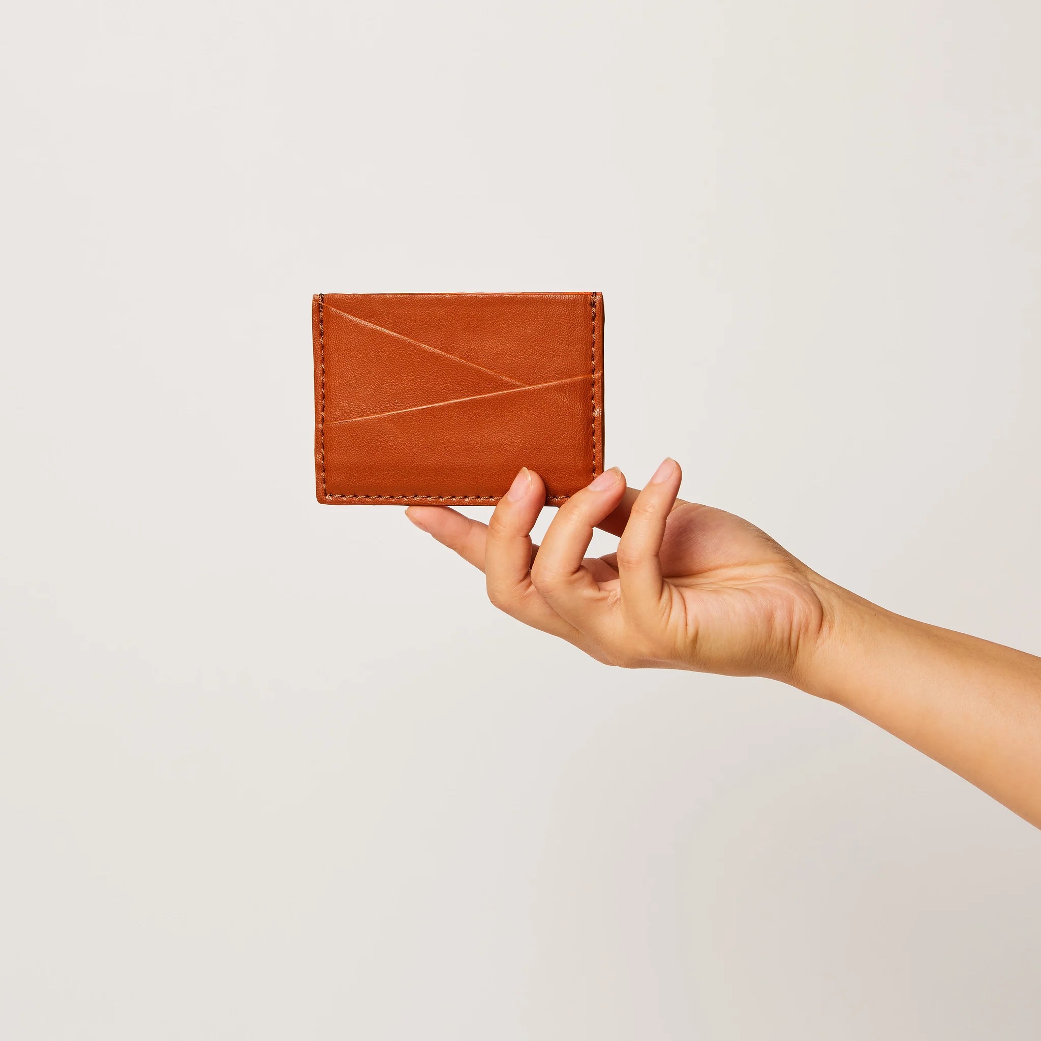 A hand holds out a brown wallet.