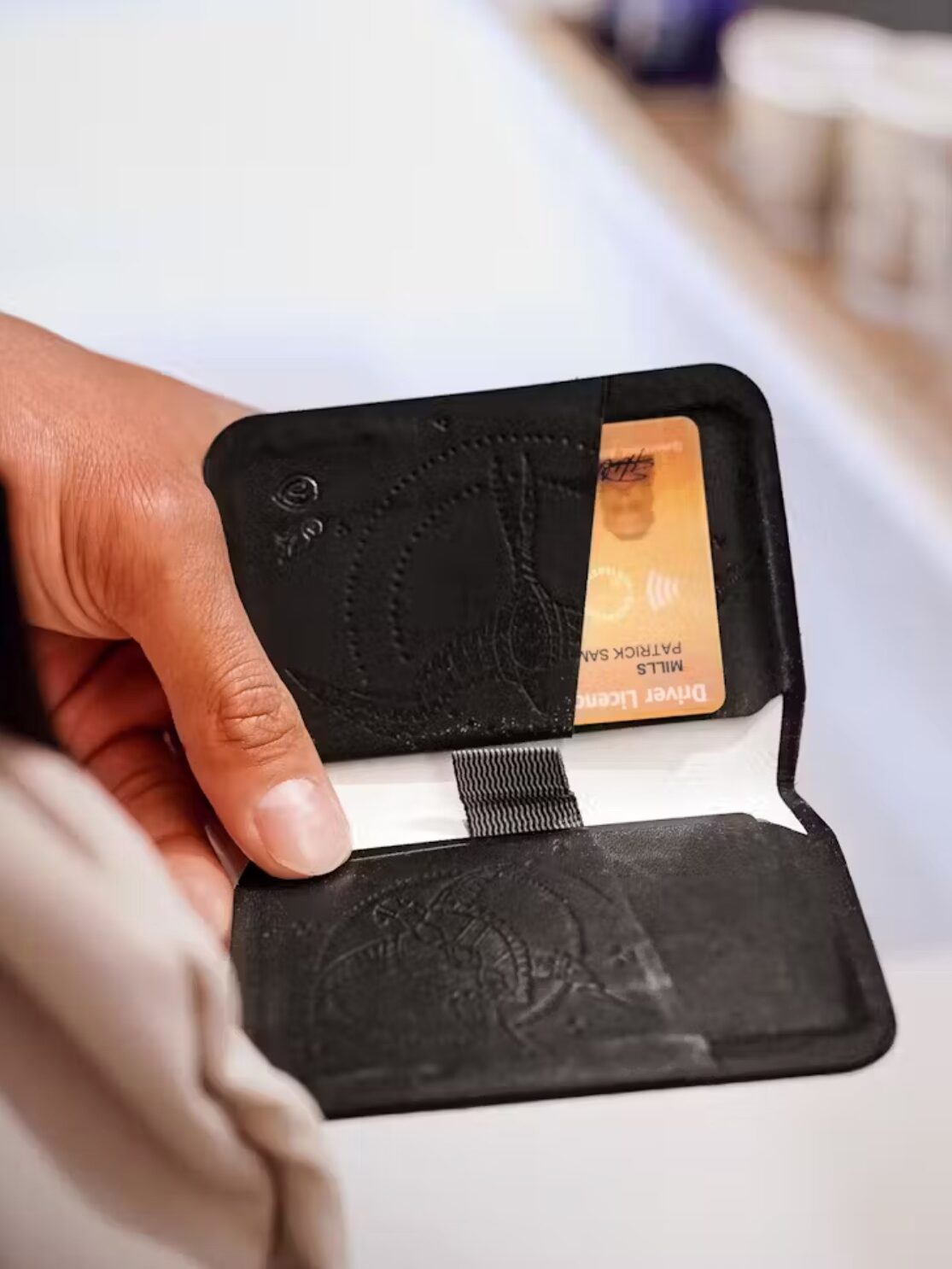 Close up of a hand holding a black slim wallet open. 