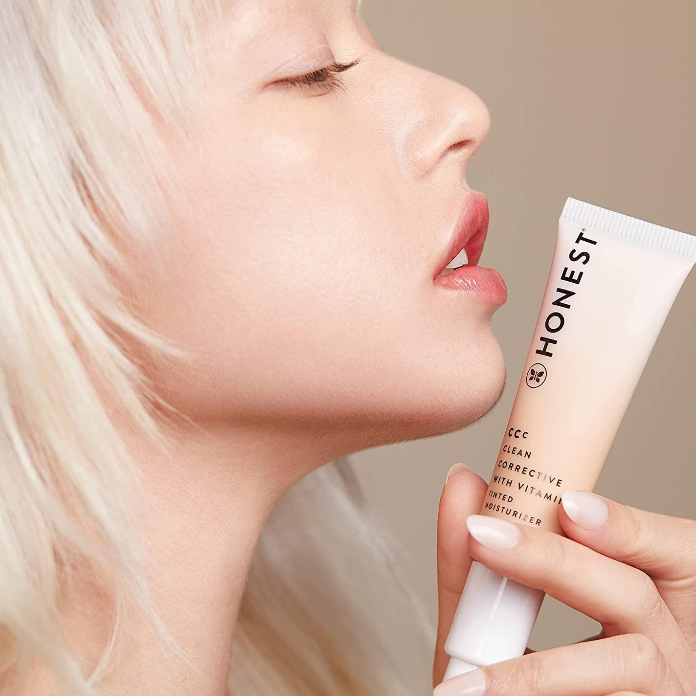 A close up of a model holding a tube of CC cream close to her chin.