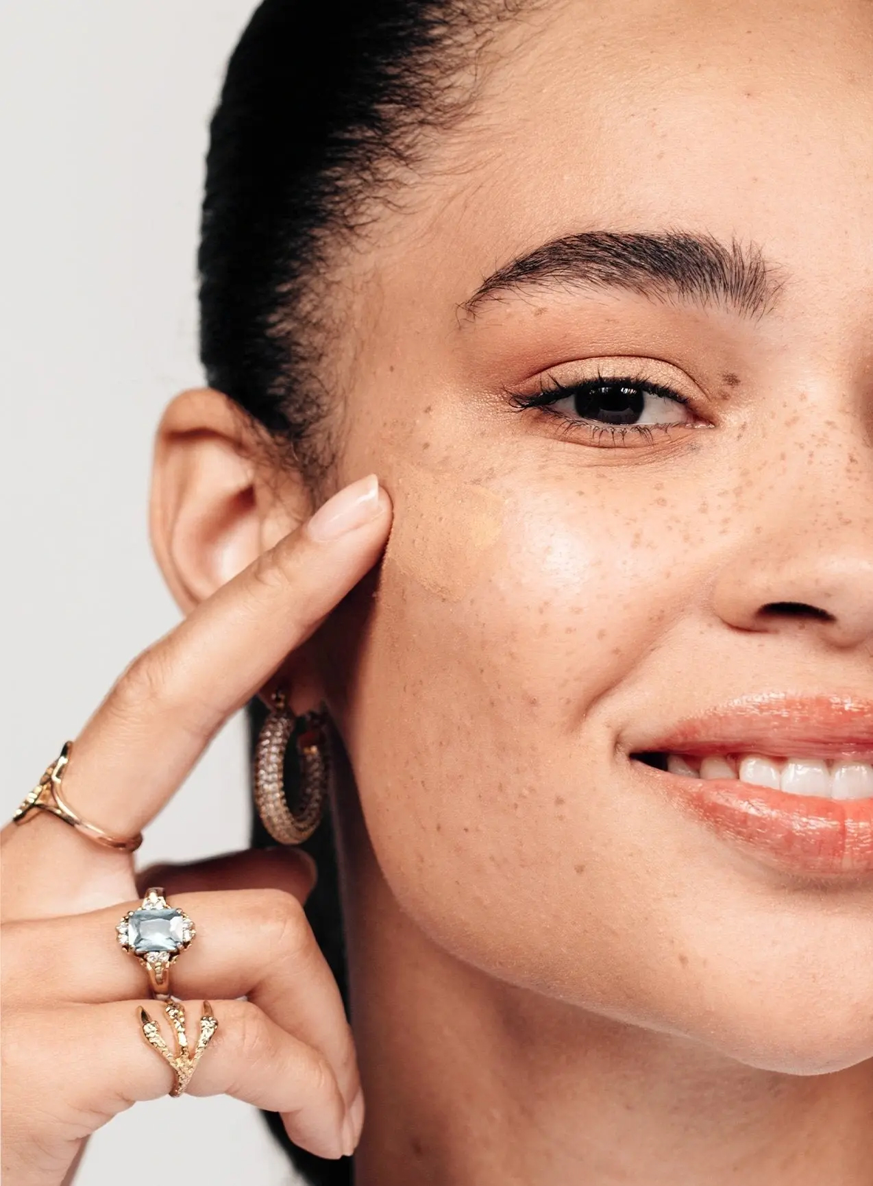 A close up of a model wiping CC cream to her cheekbone.