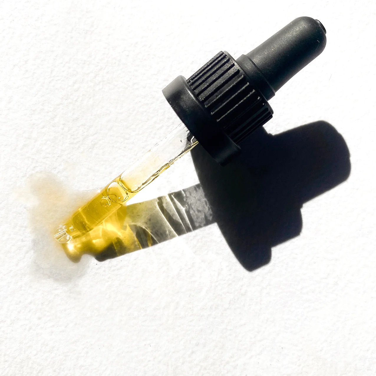 A dropper with some golden serum in it sits on a white surface.