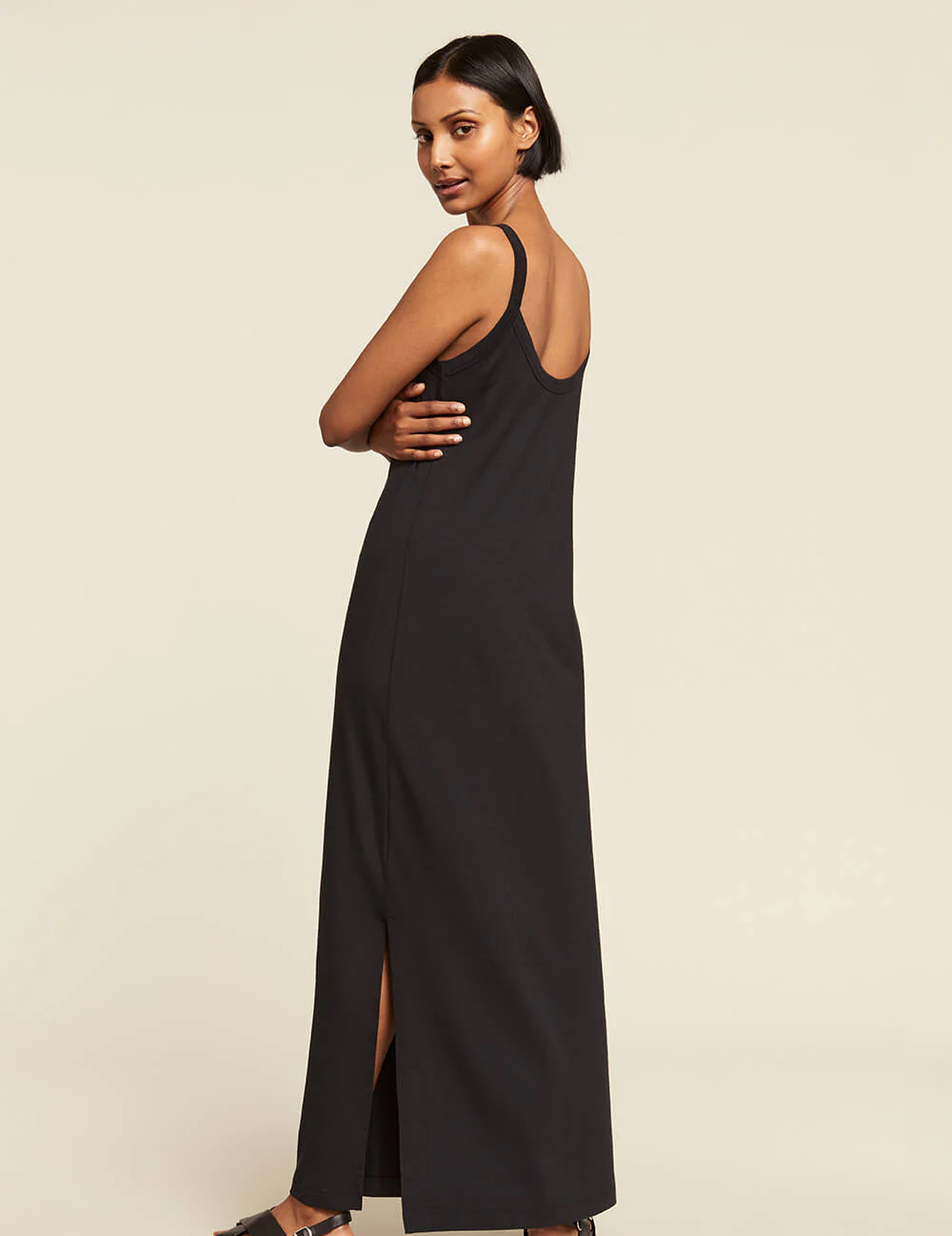 A model in a black floor length slip dress looks over her shoulder.
