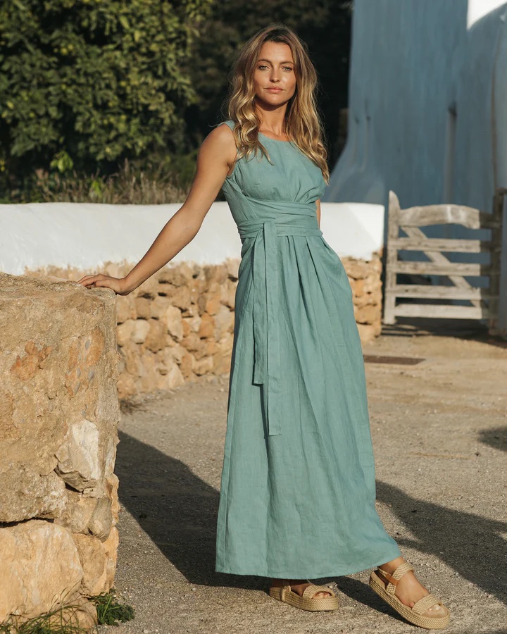 A model wears a teal linen dress with pleated bodice and tie at the waist.