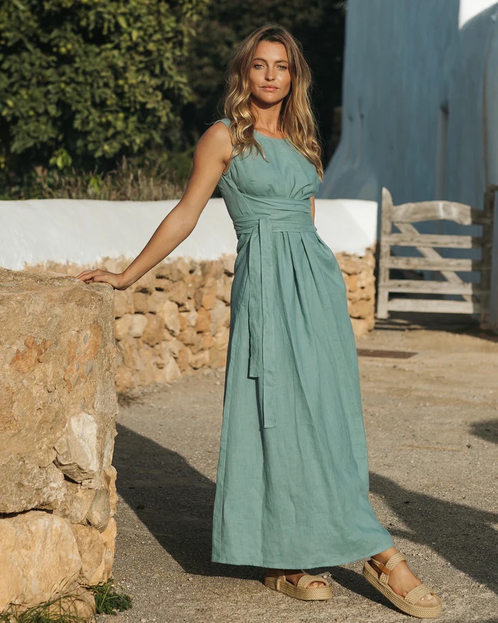 A model wears a teal linen dress with pleated bodice and tie at the waist. 