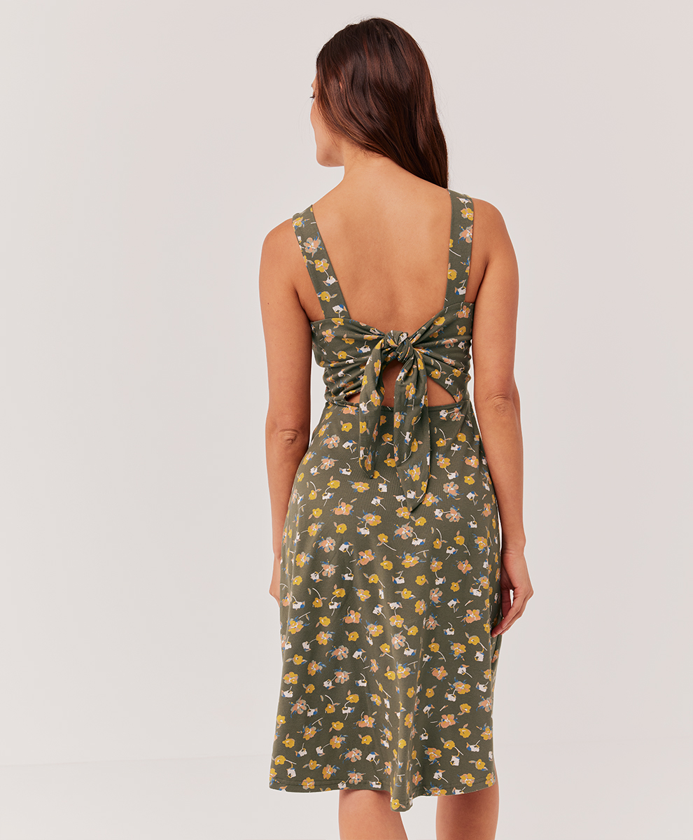 A model faces away, showing off the back tie of her green floral dress. 