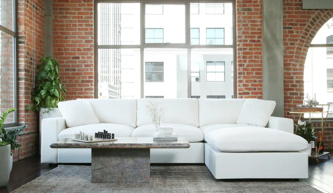 A 7th Avenue sofa modular sofa in white, set up in a loft-style apartment in front of a brick wall.