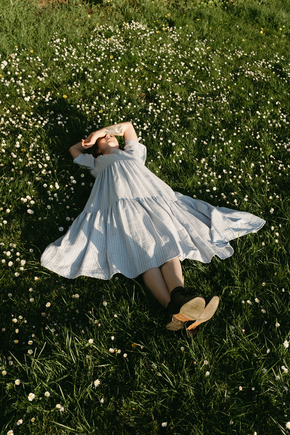A girl laying the the grass on a sunny day at the park.